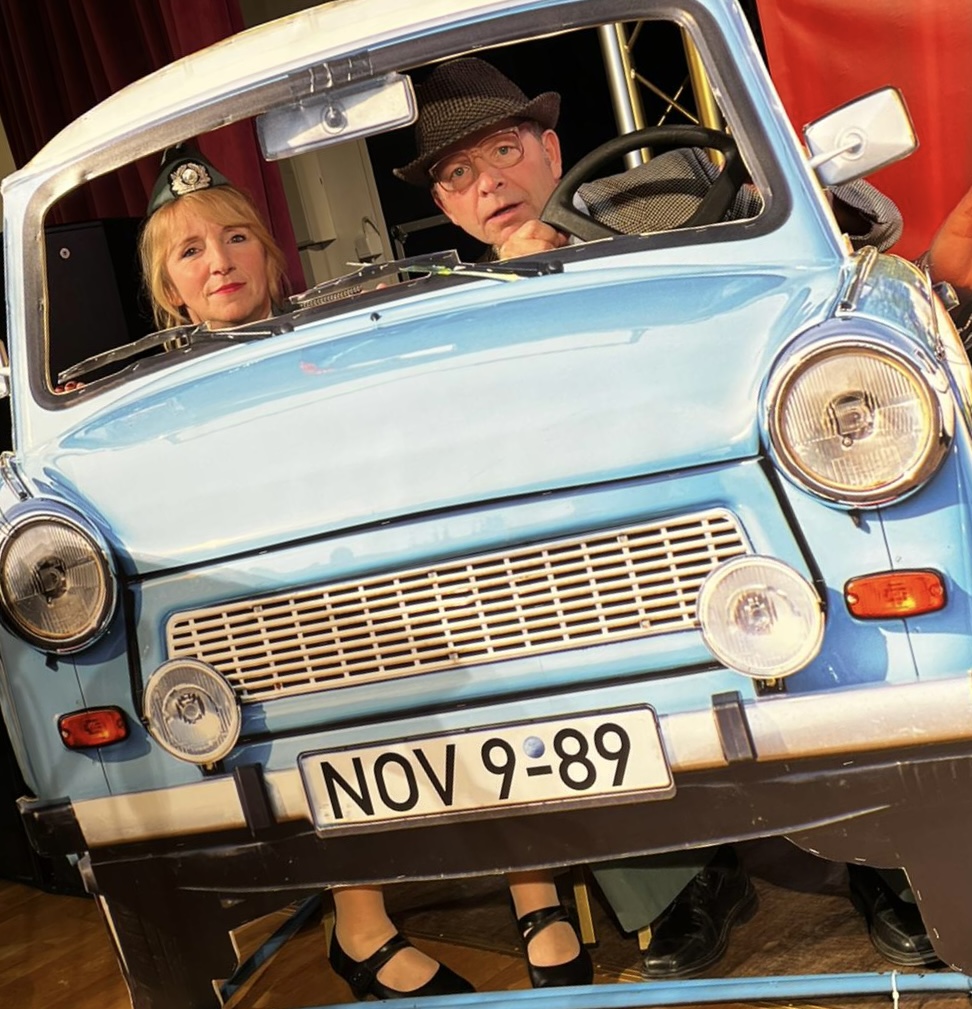 DDR Comedy Show – Volkspolizistin und Mann mit Hut in einem hellblauen Trabant mit Kennzeichen NOV 9-89